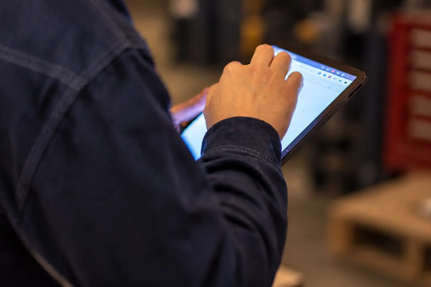 A person in a work jacket holding a tablet in a workshop, entering a record.